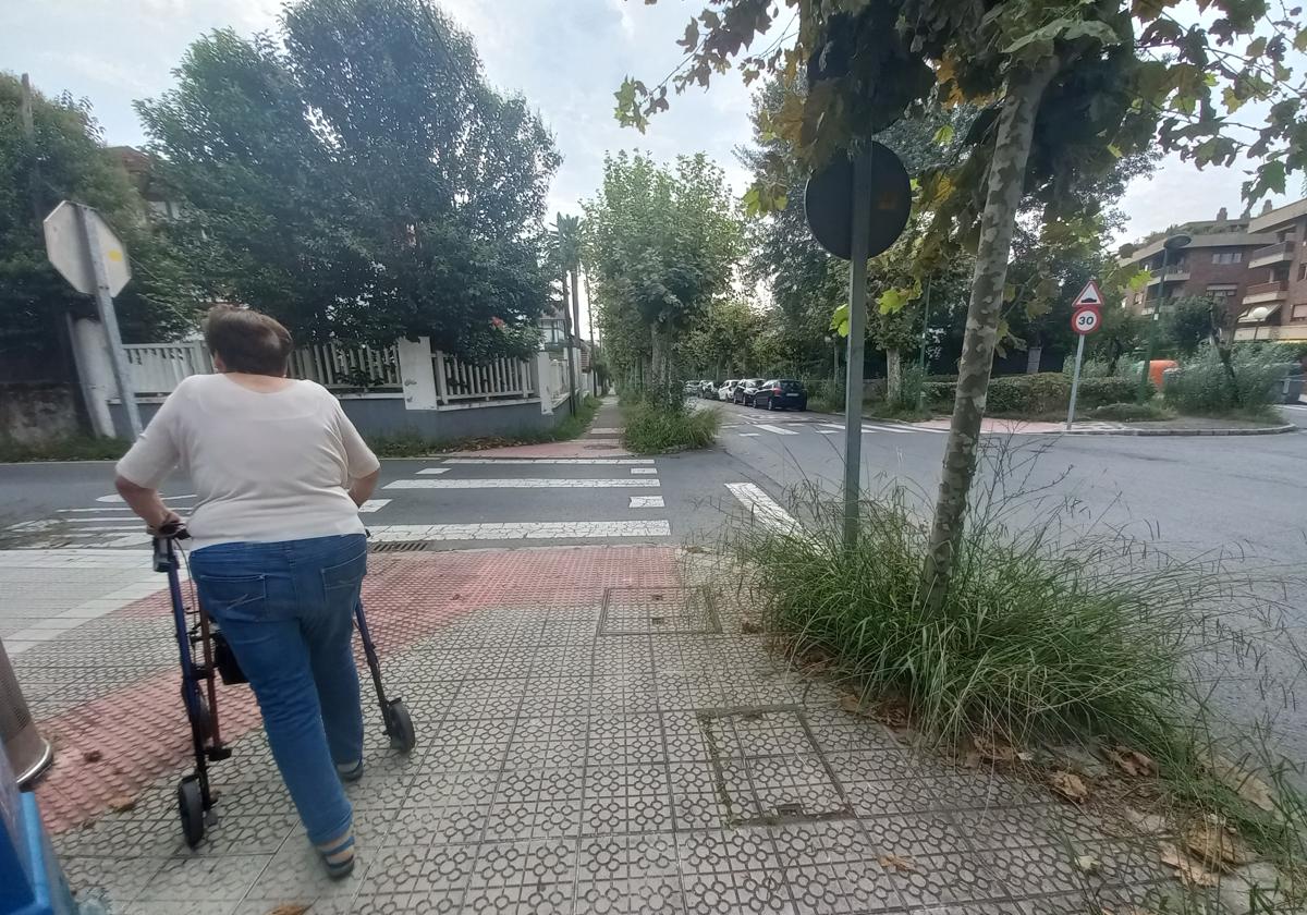 Una vecina de Neguri pasea por una acera donde la vegetación lleva tiempo sin mantenimiento.