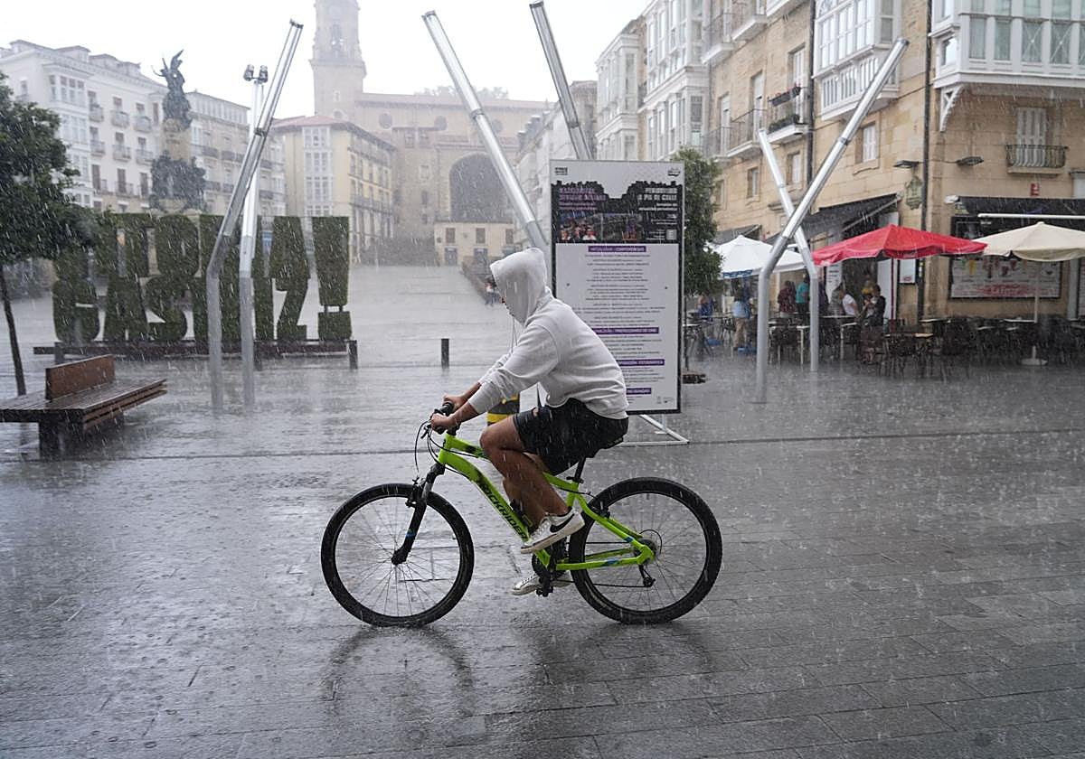 Un joven pedalea por la plaza de la Virgen Blanca bajo un intenso aguacero.