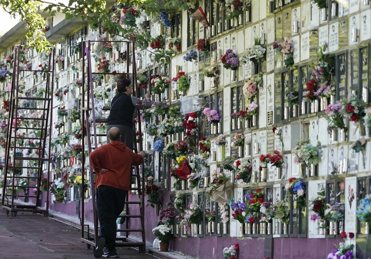 Dos personas engalanan una lápida en el cementerio de Derio.