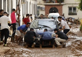 Varias personas rtiran un vehículo atrapado entre el lodo, en el barrio de La Torre, en Valencia