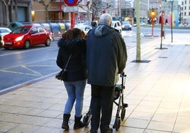 Una auxiliar acompaña a una persona mayor en su paseo.