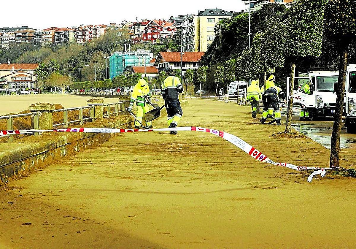 Imagen principal - Arriba, la arena de la playa de Ereaga cubrió el paseo y la carretera que discurren en paralelo al arenal. Abajo a la izquierda, nieve en el puerto de Herrera. Y a la derecha, el viento y la lluvia volvieron ayer a ser protagonistas. 