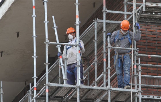 Dos operarios de una empresa de reformas realizan obras en una fachada de un edificio de Getxo.