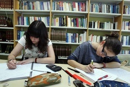 Dos jóvenes estudian en una biblioteca para preparar los exámenes.