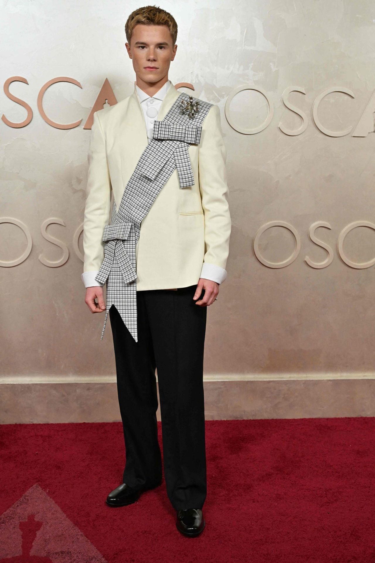 El actor sueco Edvin Ryding sorprende con una americana beige que incluye una banda con cuadros, broche y lazos. Una apuesta diferente, sin duda.