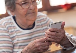 Una mujer mayor sostiene un teléfono móvil.
