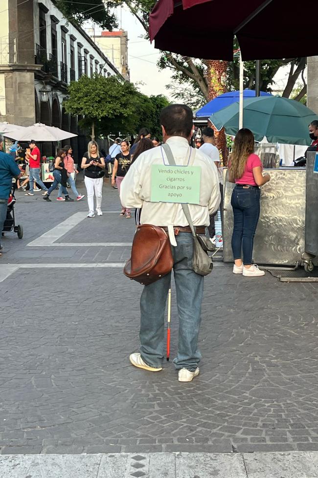 Un invidente con un cartel que pone 'Vendo chicles y cigarros. Gracias por su apoyo'.
