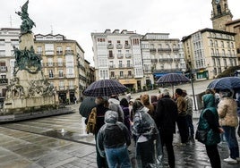 Un grupo de turistas atiende bajo la lluvia las explicaciones de un guía en la plaza de la Virgen Blanca.