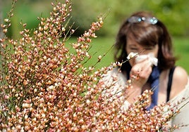 Una mujer alérgica se cubre la nariz al encontrarse cerca de una planta que arroja polen al ambiente.