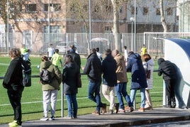 Un grupo de adultos contempla un partido de fútbol de categoría escolar.
