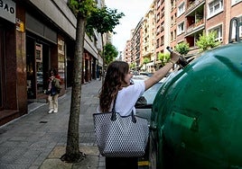Una joven deposita una botella de vidrio en un contenedor de Bilbao.