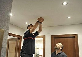 Un operario coloca en el techo de una vivienda un detector de humo.