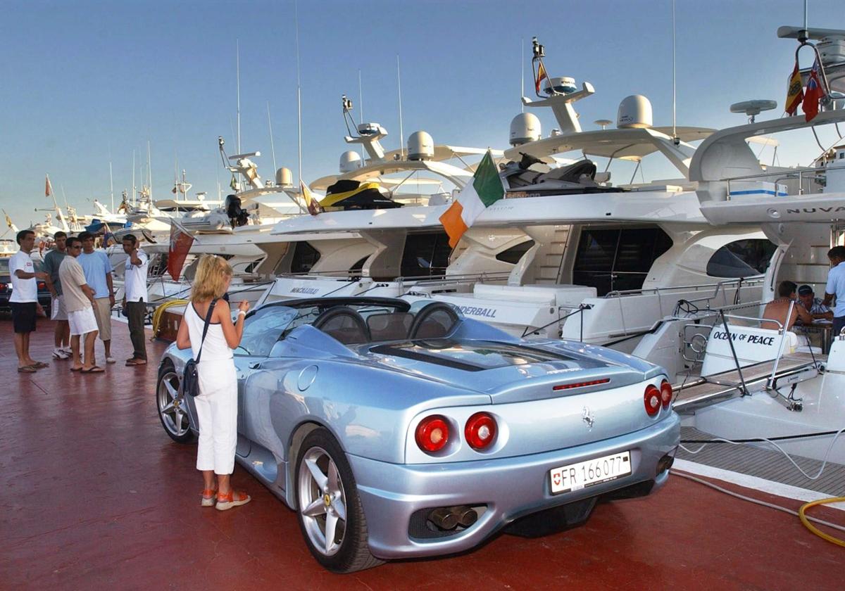Coche deportivo aparcado junto a yates de lujo en Puerto Banús.