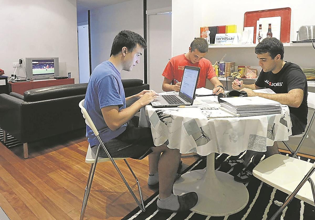 Tres estudiantes hacen sus tareas en un piso compartido.