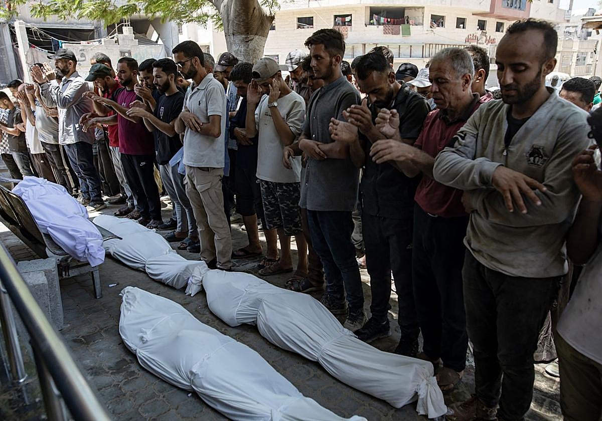 Palestinos rezan sobre los cadáveres de personas que fueron asesinadas a tiros en un punto de distribución de alimentos, en el Hospital Al-Shifa en Gaza, el 20 de julio de 2025.