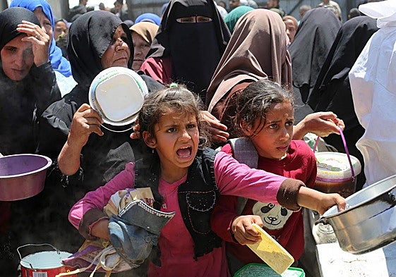 Palestinos hacen cola para recibir una comida caliente en un comedor benéfico en el campo de refugiados de Nuseirat, en el centro de la Franja de Gaza.
