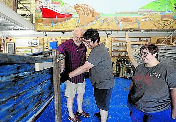 Javier, voluntario de Erain, muestra a Igor y Agurtzane desperfectos en la pintura de un barco.