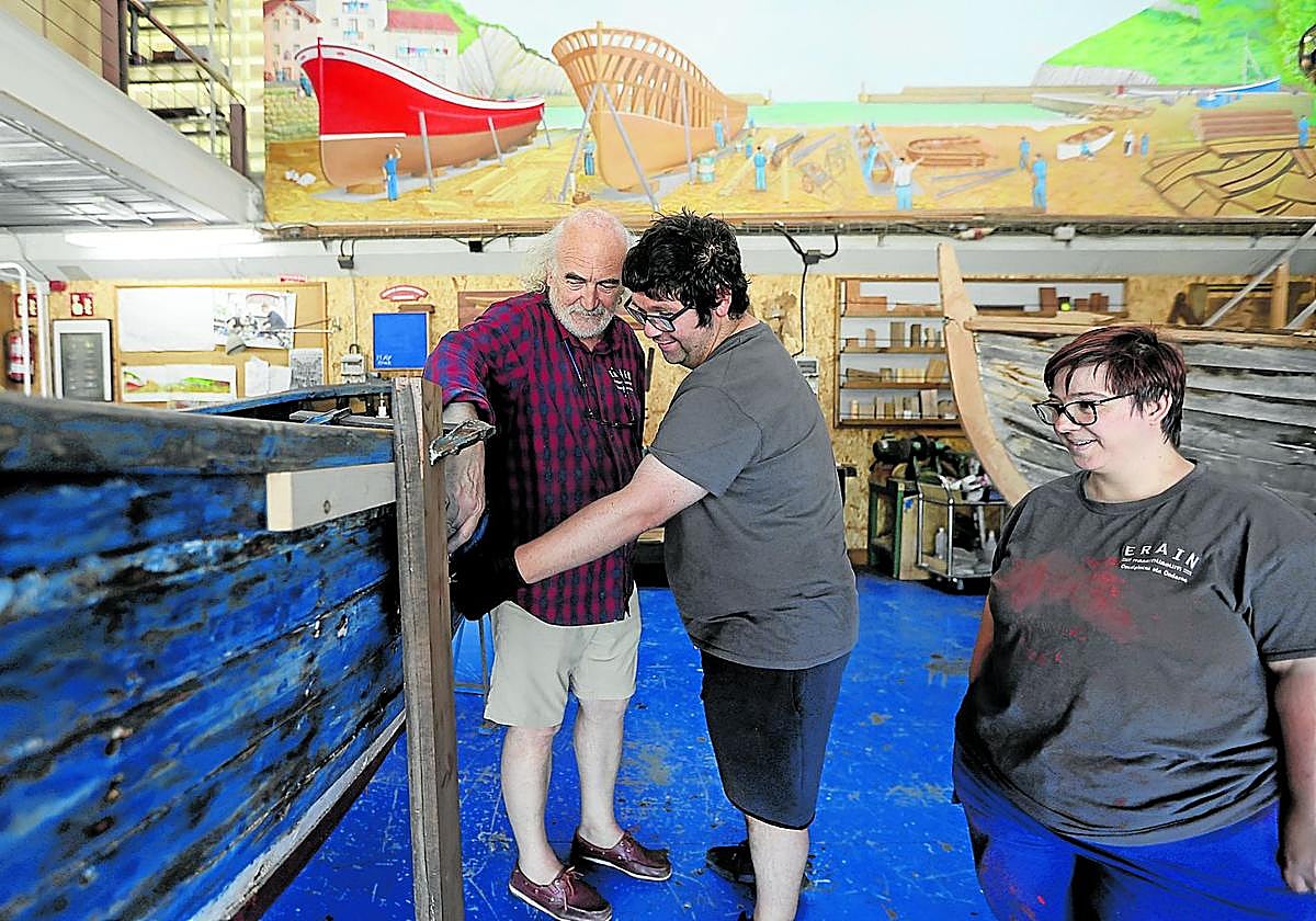 Javier, voluntario de Erain, muestra a Igor y Agurtzane desperfectos en la pintura de un barco.