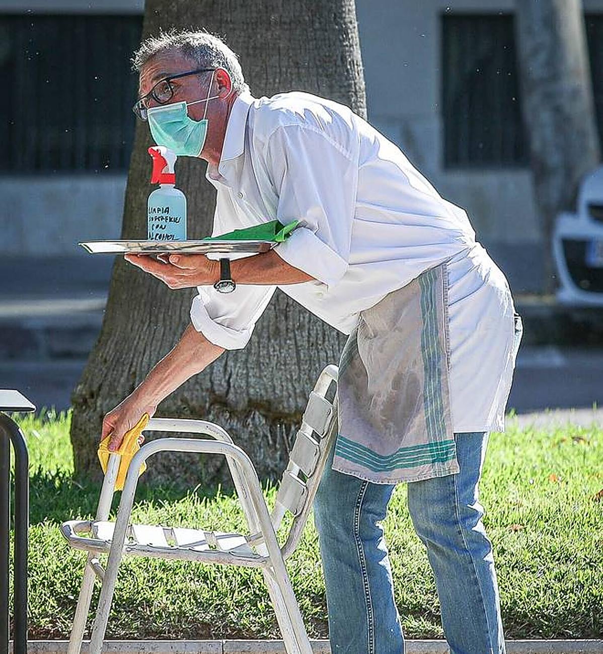 Un camarero limpia la silla de una terraza en la pandemia.
