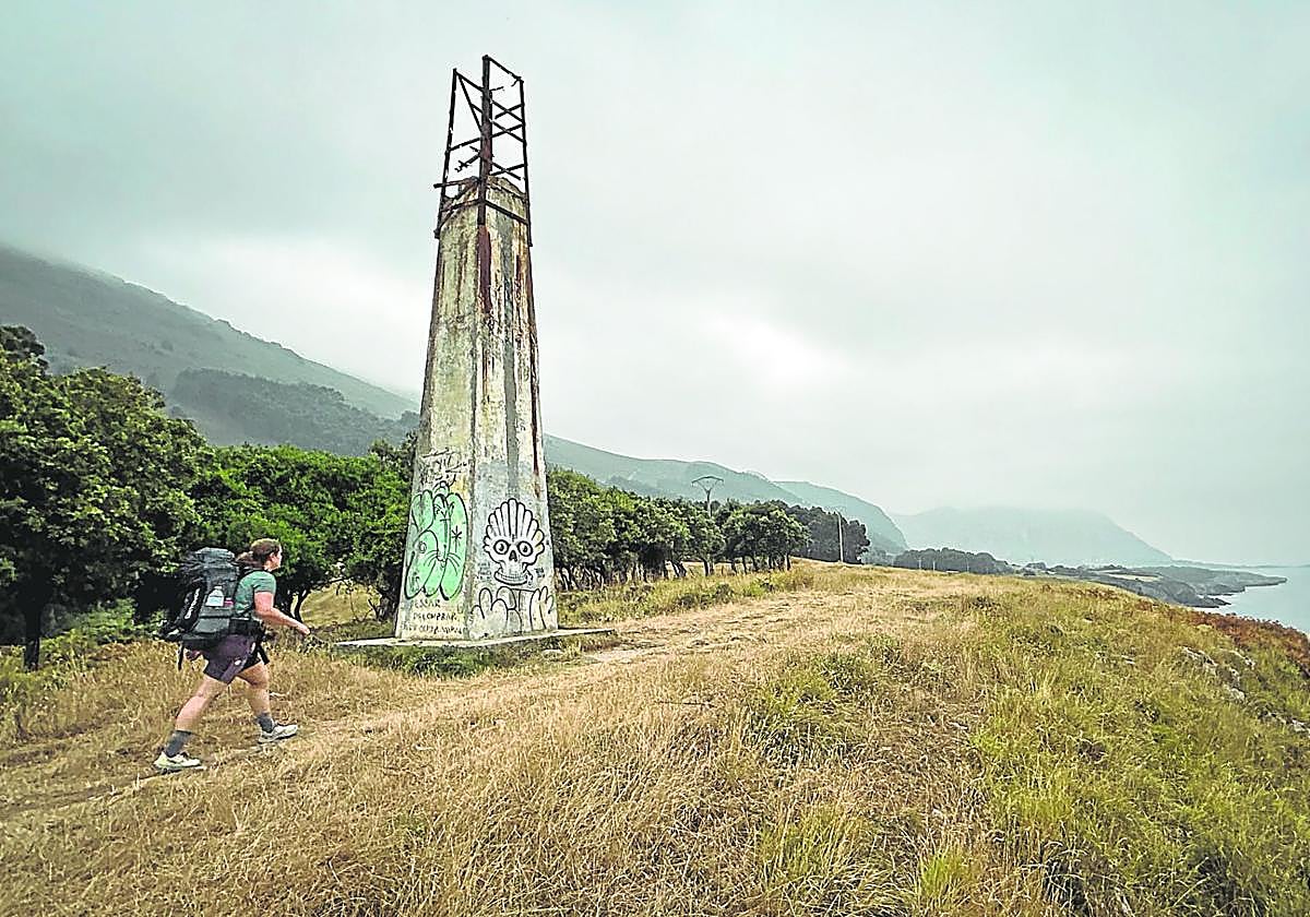Una peregina pasa junto a una torreta de la 'milla medida', flanqueada por un encinar cantábrico