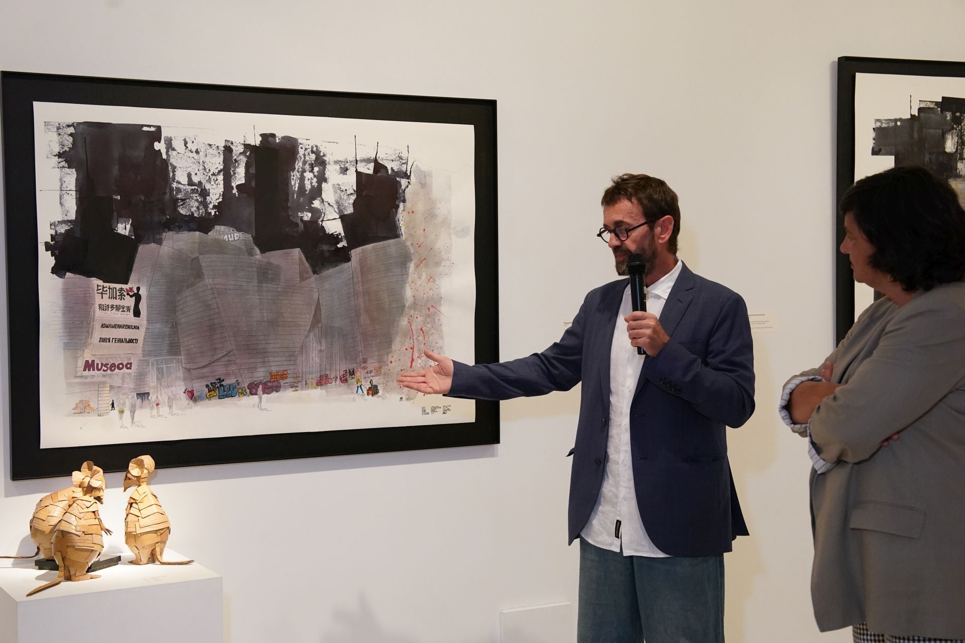 Ochoa de Olza explica a Begoña Salinas su cuadro con el Guggenheim (edificio pintado por el artista Iñaki Pardos) bajo la atenta mirada de las ratas obra de Cova Orgaz.