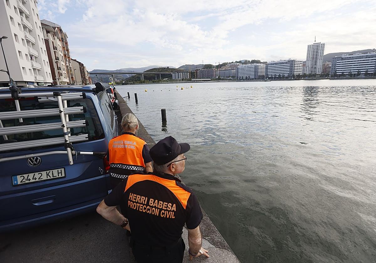 Dos integrantes de Protección Civil vigilan la Ría a la altura de Erandio, con Rontegi al fondo.