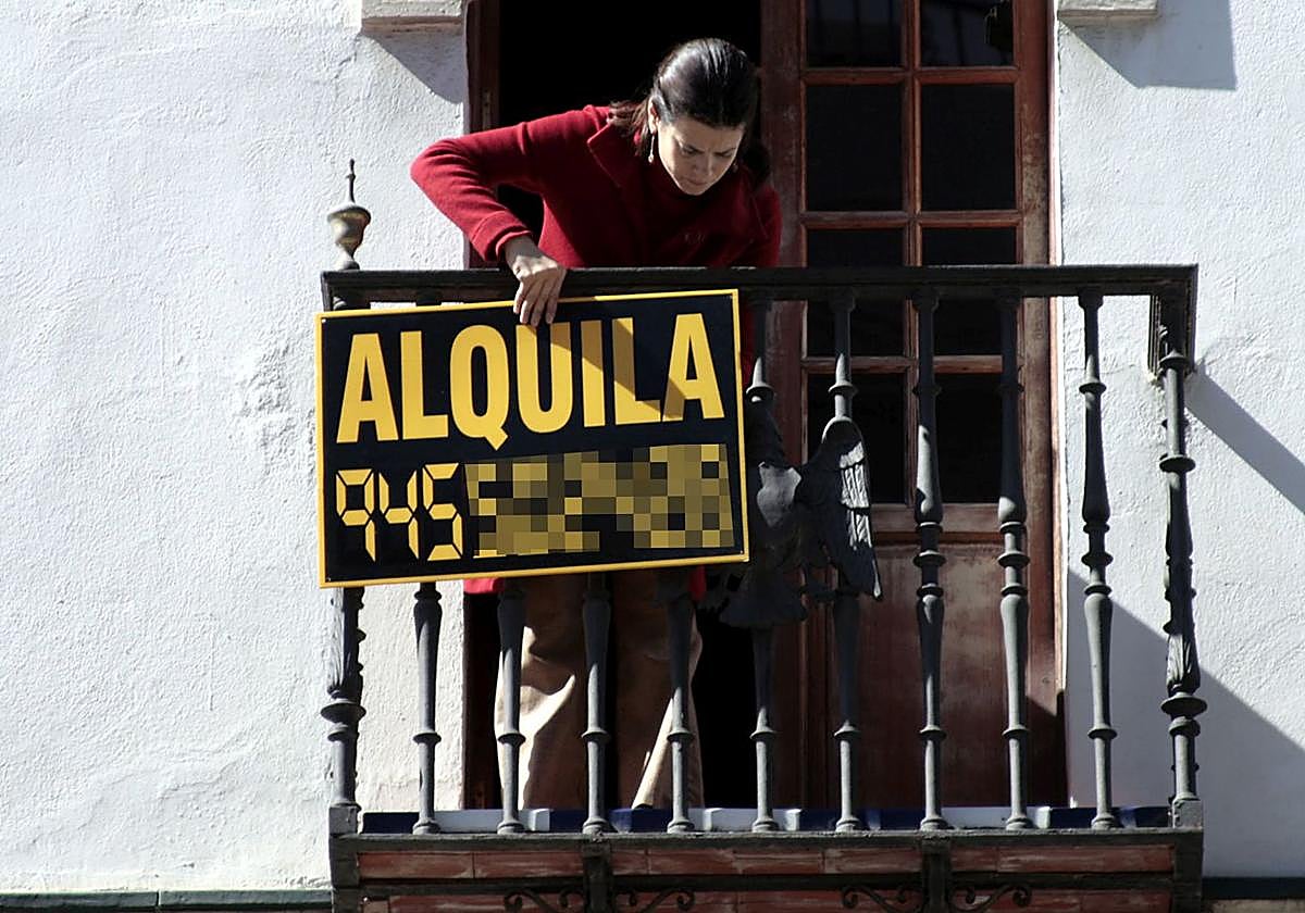 Una mujer coloca el cartel de alquiler en el balcón de una vivienda.