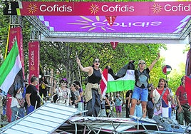 En el recorrido dos manifestantes con la bandera de Palestina protestan en el paso de un kilómetro para la meta.