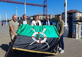 Representantes institucionales, patrocinadores y miembros del club de remo de Portugalete, con la bandera frente al Puente Colgante.