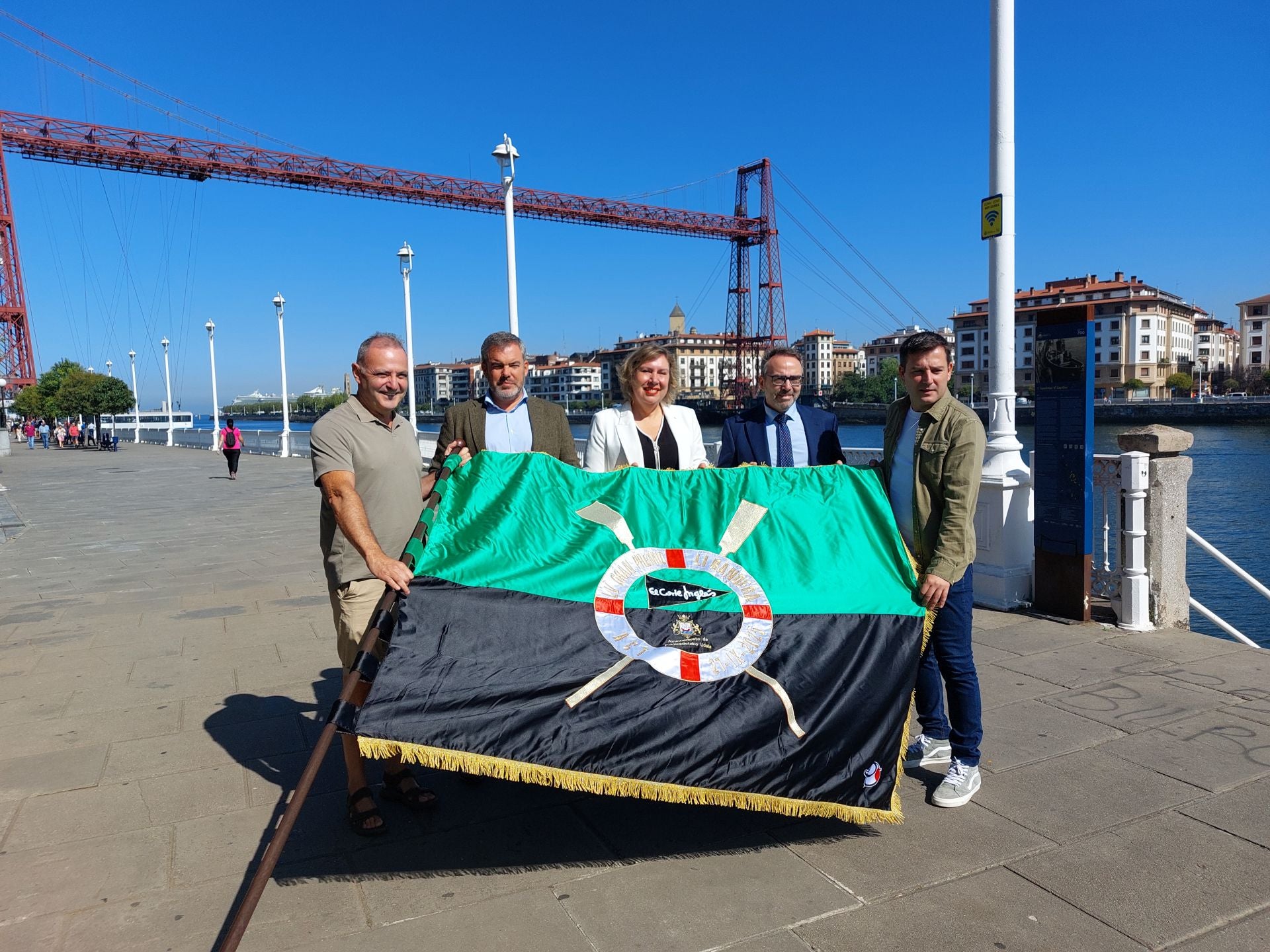 Representantes institucionales, patrocinadores y miembros del club de remo de Portugalete, con la bandera frente al Puente Colgante.