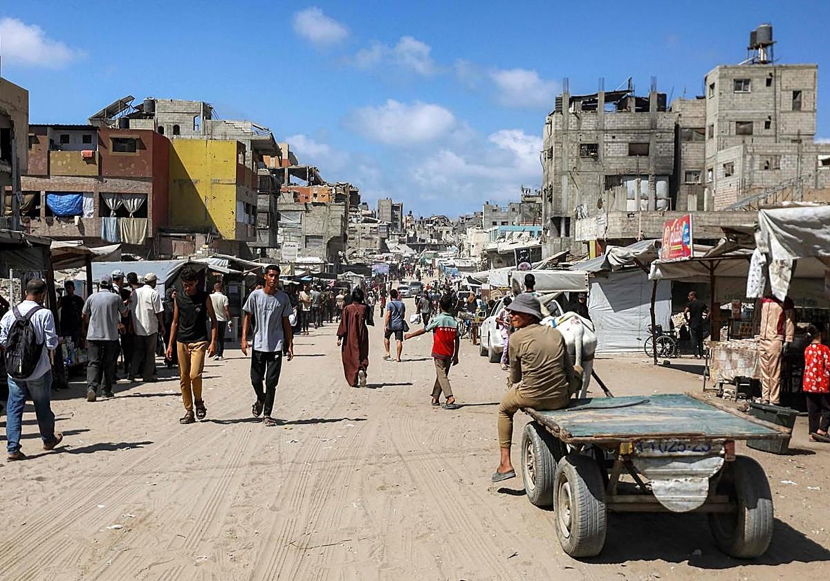 Personas caminando junto a edificios dañados a lo largo de una calle en Khan Yunis, en el sur de la Franja de Gaza.