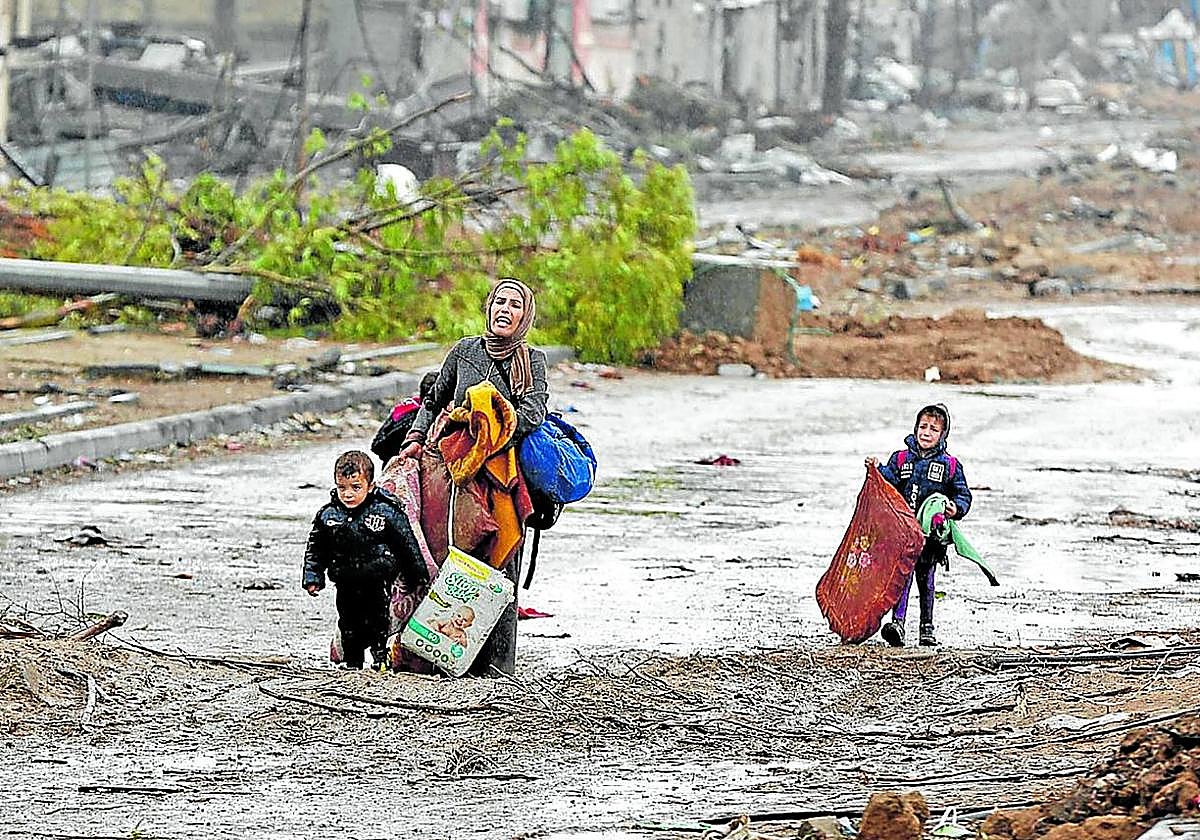 Una madre y sus dos hijos pequeños huyen a pie de Gaza entre los escombros en noviembre de 2023.