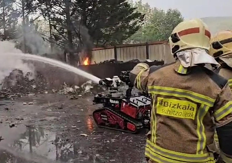 Dos profesionales y el robot tratan de apagar el fuego originado en un montón de chatarra.
