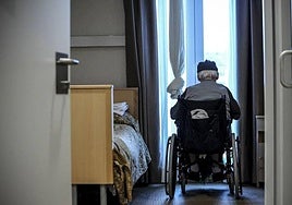 Un mayor dependiente observa por la ventana de una residencia.