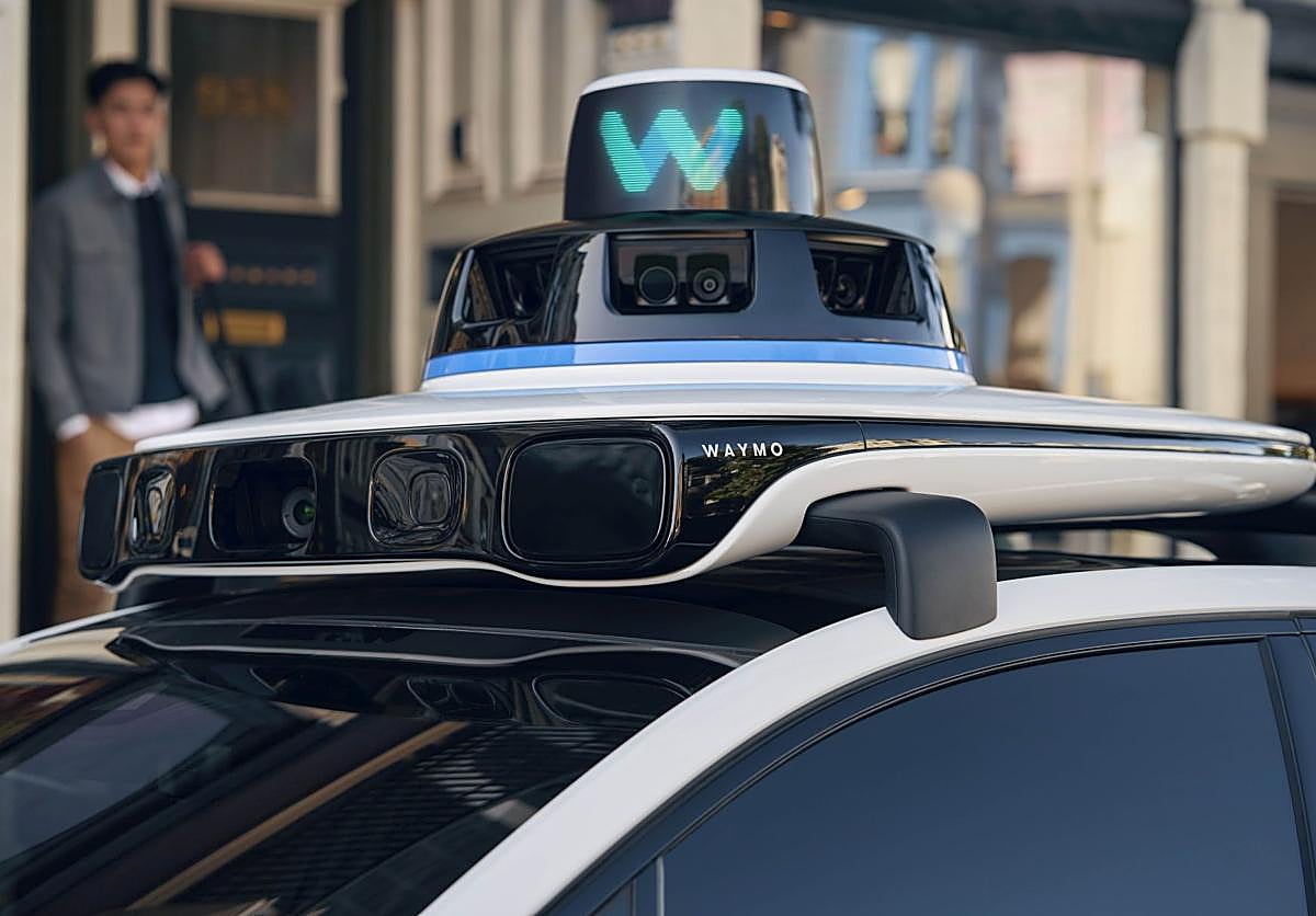 Imagen principal - Arriba a la izquierda, los sensores y cámaras en la parte superior del robotaxi; a la derecha, el coche circula sin volante y, abajo, la aplicación móvil avisa del tiempo de espera para la recogida.