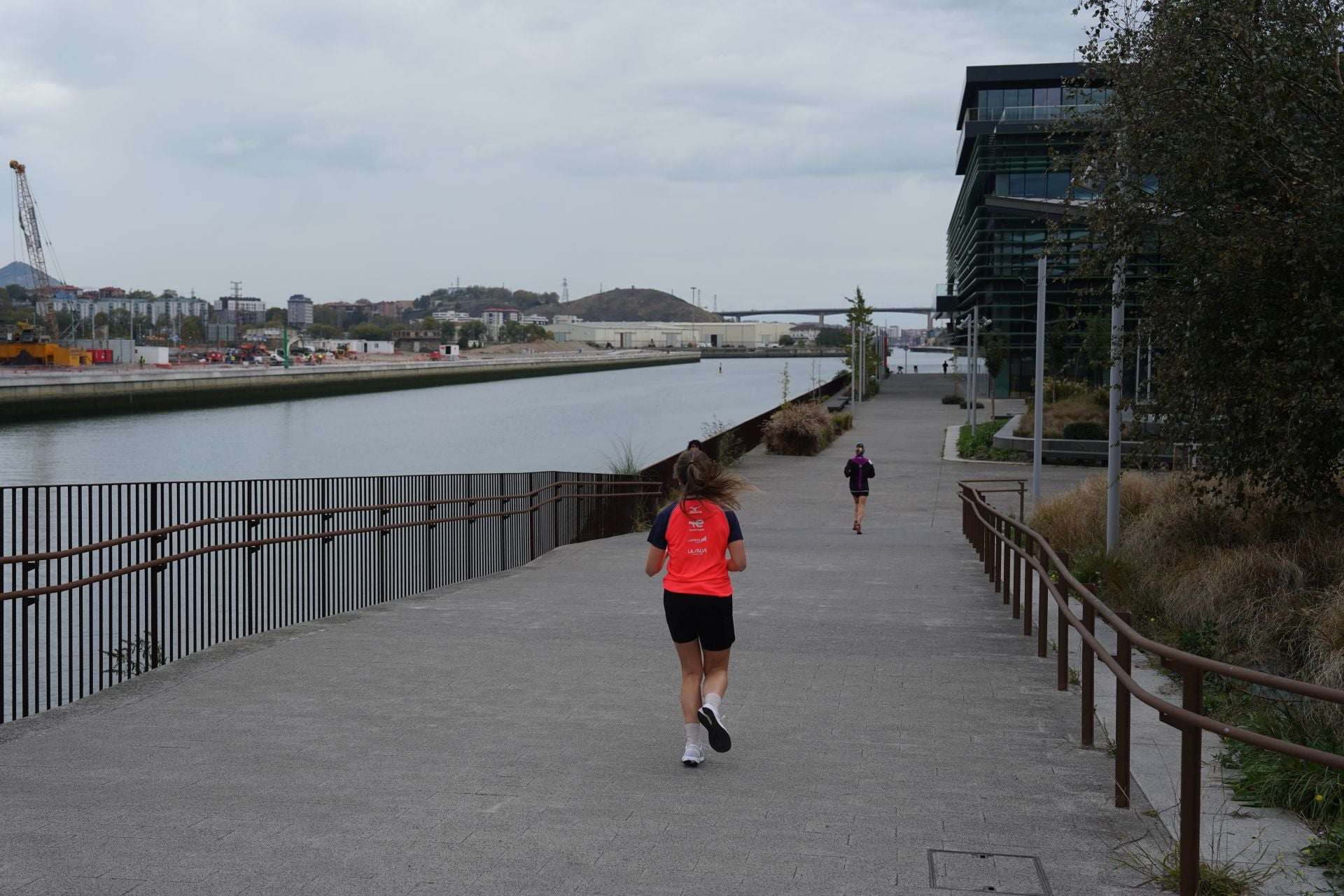 Jóvenes corren por el paseo del Canal, frente a las obras en la isla de Zorrozaurre.