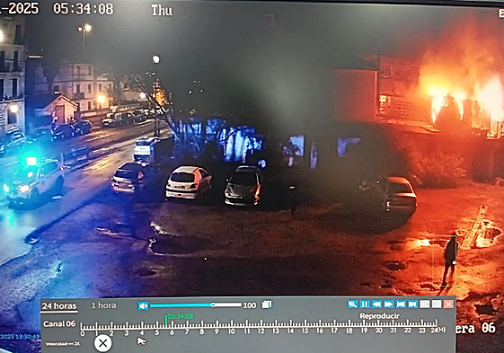 Una cámara de seguridad capta la llegada de la Ertzaintza, a las 4.34 horas, aunque el reloj marca las 5.34. A la derecha de la imagen, el vecino de la caseta de al lado observa la dimensión de las llamas.