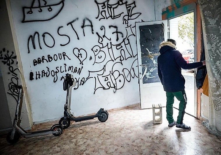 Dos patinetes en una lonja okupada de Coronación. En la puerta, un joven que declara «buscar trabajo» y que en su país era «marinero».