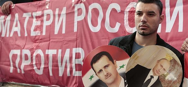 Un manifestante sostiene los retratos de Putin y El-Asad / REUTERS/Tatyana Makeyeva