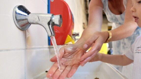 Una mujer enseña a un niño a lavarse las manos.