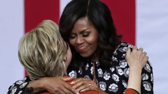 Michelle Obama y Hillary Clinton se abrazan.