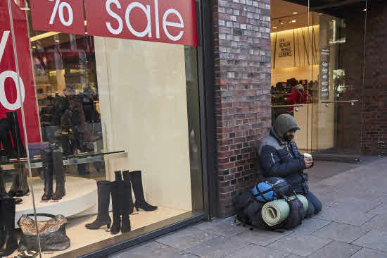 Un hombre pide dinero frente a una tienda. 