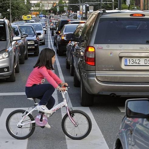 Una niña cruza una calle  por el paso de cebra con su bicicleta.