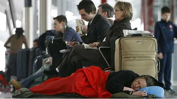 Una mujer duerme en el suelo de la terminal de un aeropuerto.