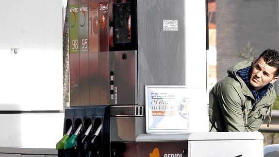 Un conductor mira el contador mientras reposta en una estación de servicio. 