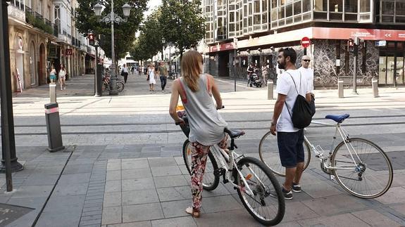 Dos ciclistas, bici en mano, por en centro peatonal. 
