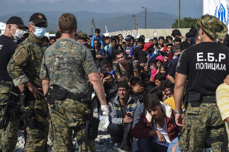 Policías macedonios vigilan a los refugiados que esperan para poder subir a un tren con dirección a Serbia.