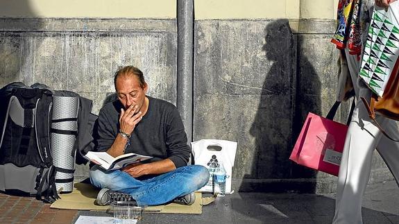 Jose fuma y lee mientras pide una limosna en la Gran Vía de Bilbao. 
