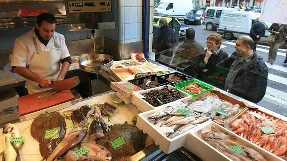 Clientes contemplan el género expuesto en el escaparate de una pescadería de Bilbao.