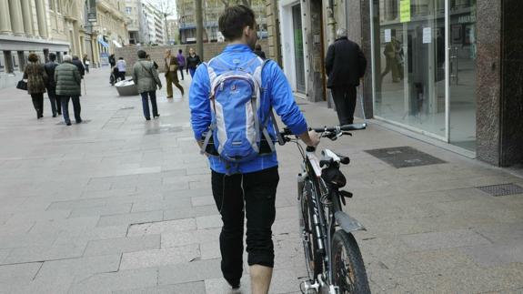 Un ciclista camina con su bicicleta por la calle Postas